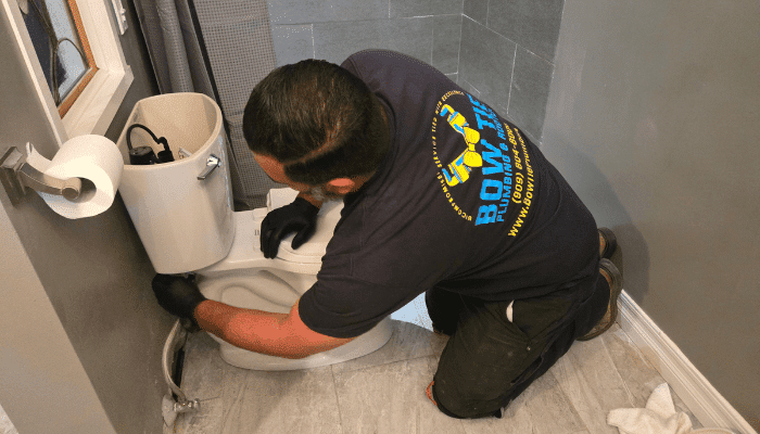 Bow Tie Plumber working to fix a toilet.