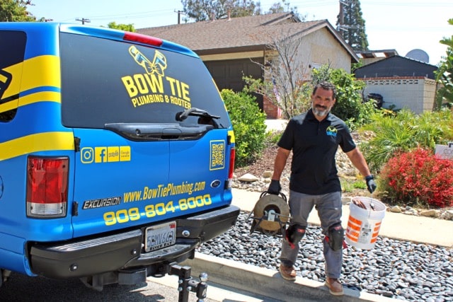 ow Tie Plumbing & Rooter owner and technician loading plumbing equipment into his work truck in Rancho Cucamonga, CA