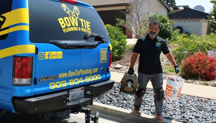 Bow Tie Plumber Walking Back To Truck With Drain Clearing Equipment